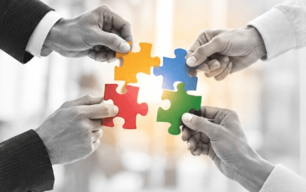 Four hands joining colorful puzzle pieces